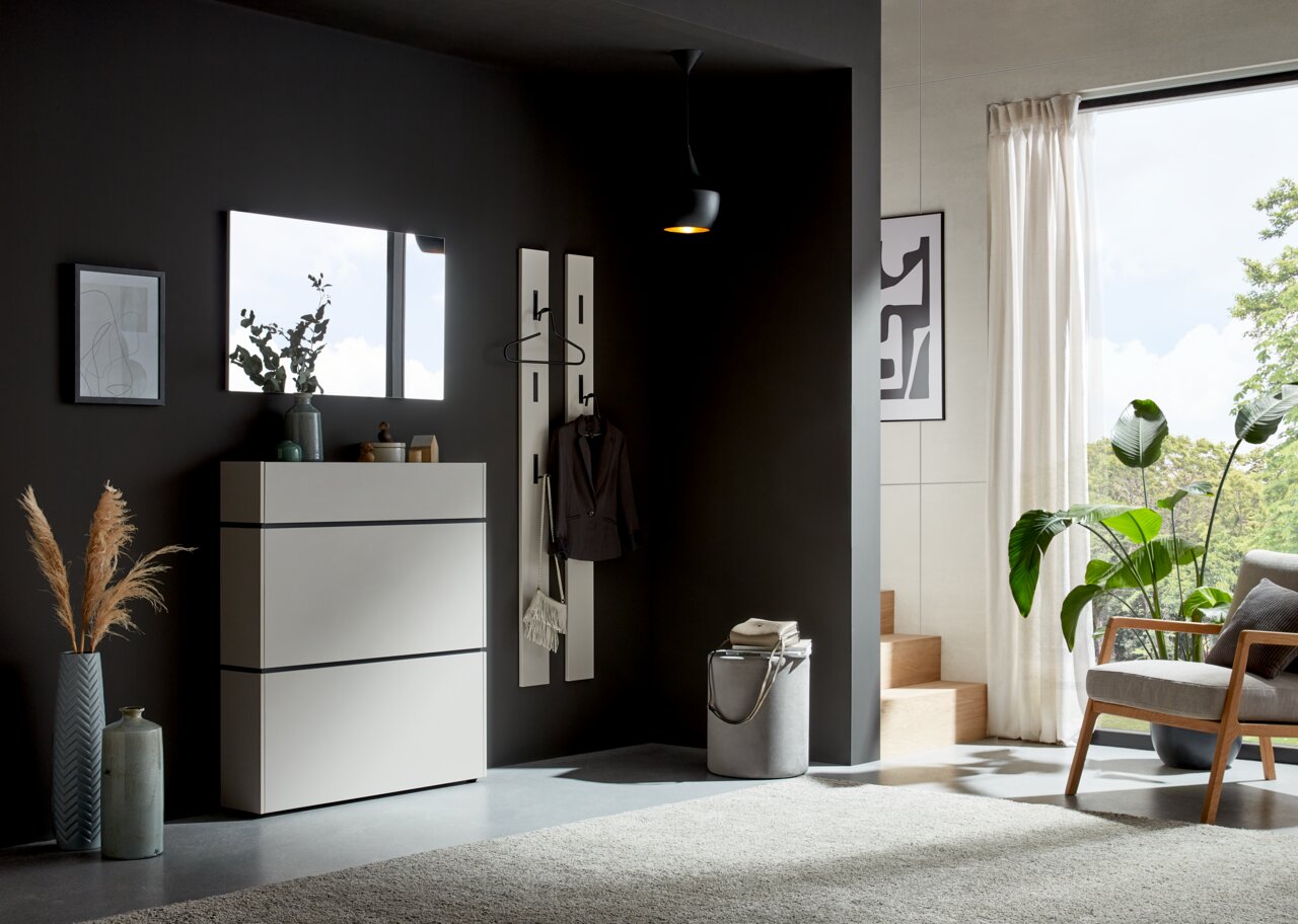 Voleo Garderobenpaneel UNIQUE Moderner Eingangsbereich mit einem weißen Schuhschrank, einem rechteckigen Spiegel und einem Garderobenpaneel an einer dunklen Wand. Perspektive von vorne.