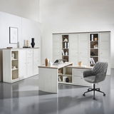 Moderner Eckschreibtisch in heller Holzoptik mit integriertem Stauraum, umgeben von passenden Schränken und einem grauen Bürostuhl, aus der Perspektive eines Betrachters im Raum.