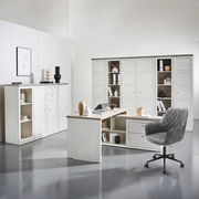 Moderner Eckschreibtisch in heller Holzoptik mit integriertem Stauraum, umgeben von passenden Schränken und einem grauen Bürostuhl, aus der Perspektive eines Betrachters im Raum.