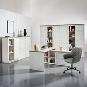 Modern hoekbureau in lichte houtlook met ingebouwde opbergruimte, omringd door bijpassende kasten en een grijze bureaustoel, gezien vanuit het perspectief van iemand die in de kamer staat.