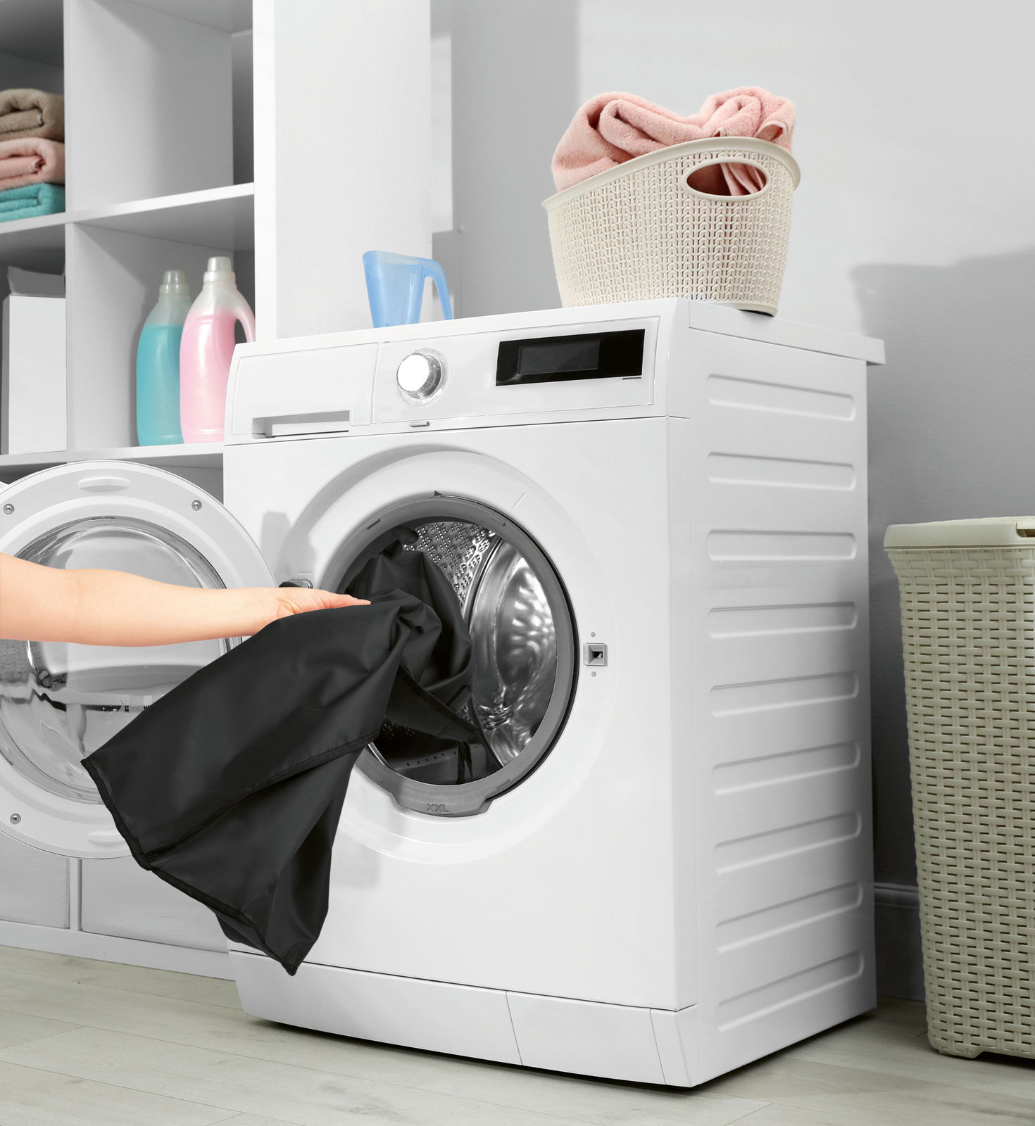 Frontansicht einer modernen Waschmaschine mit geöffneter Tür, in die eine Person schwarze Wäsche legt. Oben auf der Maschine steht ein Korb mit gefalteten Handtüchern.