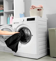 Frontansicht einer modernen Waschmaschine mit geöffneter Tür, in die eine Person schwarze Wäsche legt. Oben auf der Maschine steht ein Korb mit gefalteten Handtüchern.