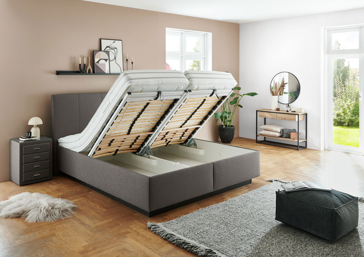 Modernes Polsterbett mit hochgeklappten Lattenrosten, seitliche Perspektive, in einem stilvoll eingerichteten Schlafzimmer mit Holzboden und großen Fenstern.