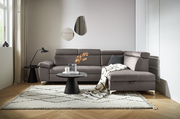 Moderne graue Rundecke in einem stilvoll eingerichteten Wohnzimmer, von vorne betrachtet. Die Couch ist mit einem Kissen und einer Decke dekoriert, umgeben von einem Teppich, einem Couchtisch und einer Stehlampe.