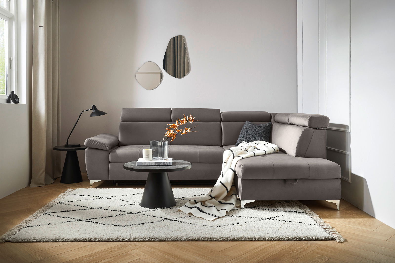 Moderne graue Rundecke in einem stilvoll eingerichteten Wohnzimmer, von vorne betrachtet. Die Couch ist mit einem Kissen und einer Decke dekoriert, umgeben von einem Teppich, einem Couchtisch und einer Stehlampe.
