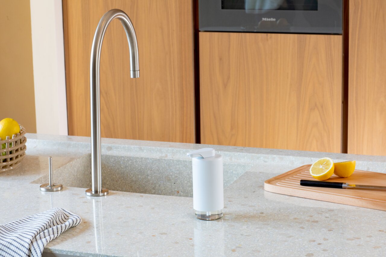 Moderner weißer Seifenspender auf einer Küchenarbeitsplatte neben einem Wasserhahn, mit Blick auf die Vorderseite des Spenders.
