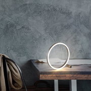 Moderne Tischleuchte RITUS in Ringform auf einem Holztisch, seitliche Perspektive