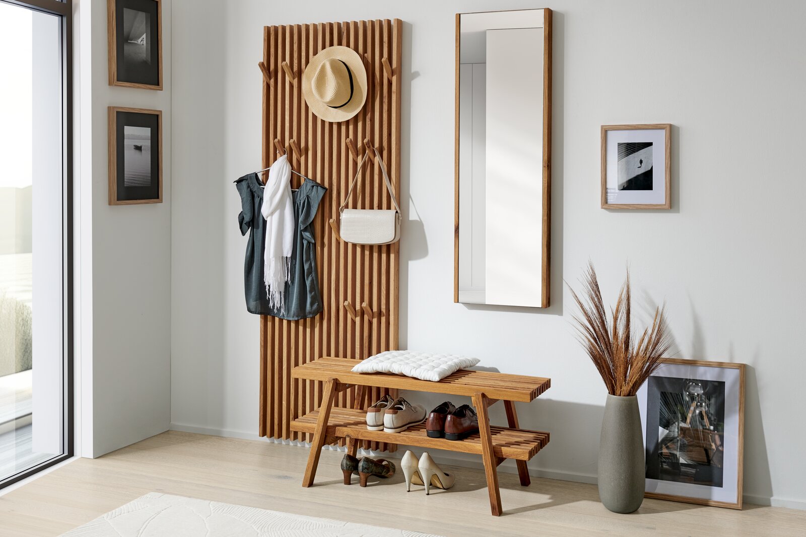 Linea Natura XL-Garderobenpaneel STUDIO LINE Holzgarderobenpaneel mit Haken, an dem Kleidung und Accessoires hängen, daneben ein Spiegel und eine Bank mit Schuhen, aus seitlicher Perspektive fotografiert.