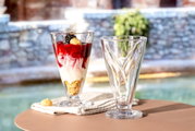 Twee hoge glazen schalen, waarvan één gevuld met een dessert, op een tafel in de open lucht, gezien vanuit de zijkant.