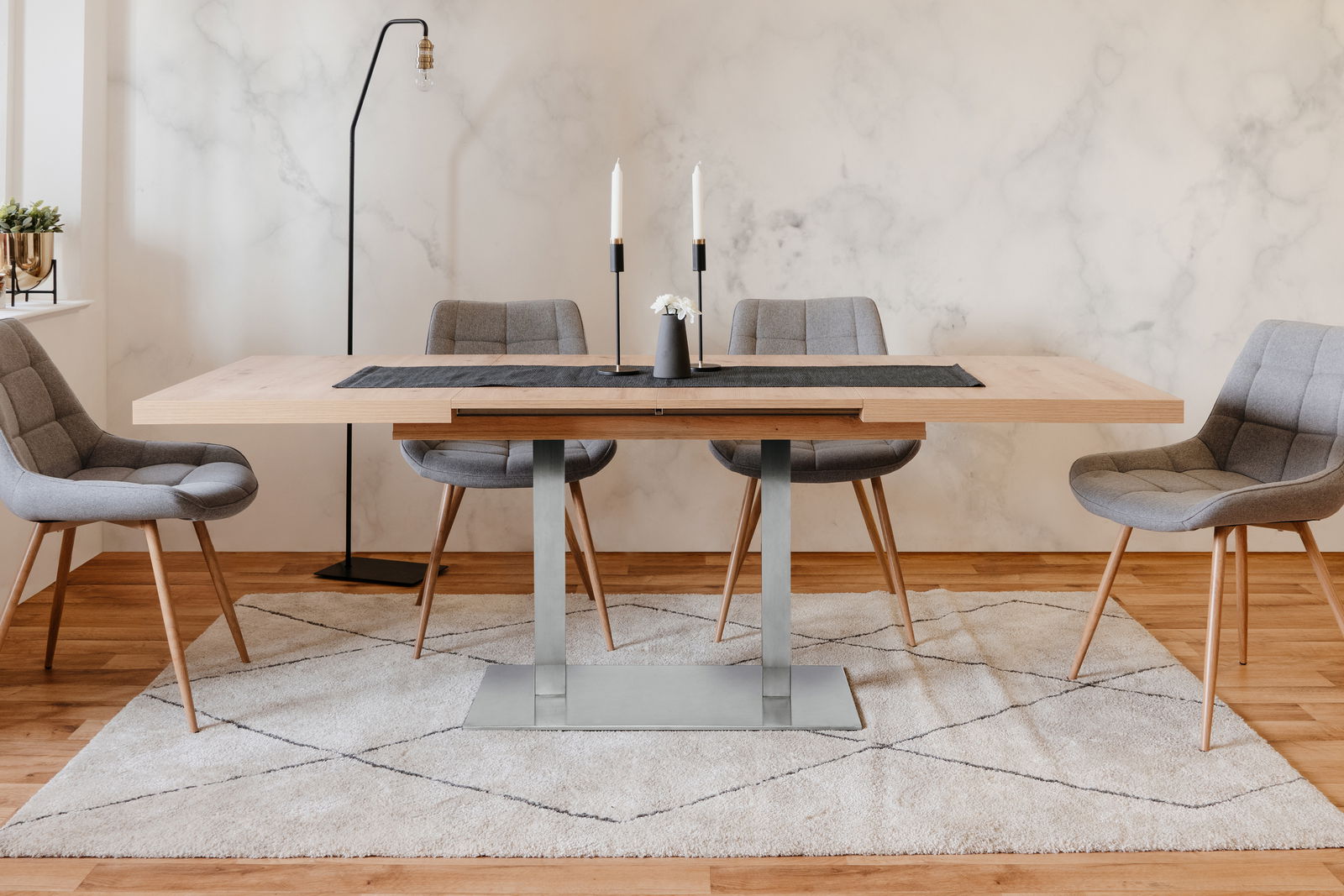 Moderner Esstisch mit Holzplatte und Metallgestell, umgeben von vier grauen Polsterstühlen, in einem stilvoll eingerichteten Raum. Frontalansicht.
