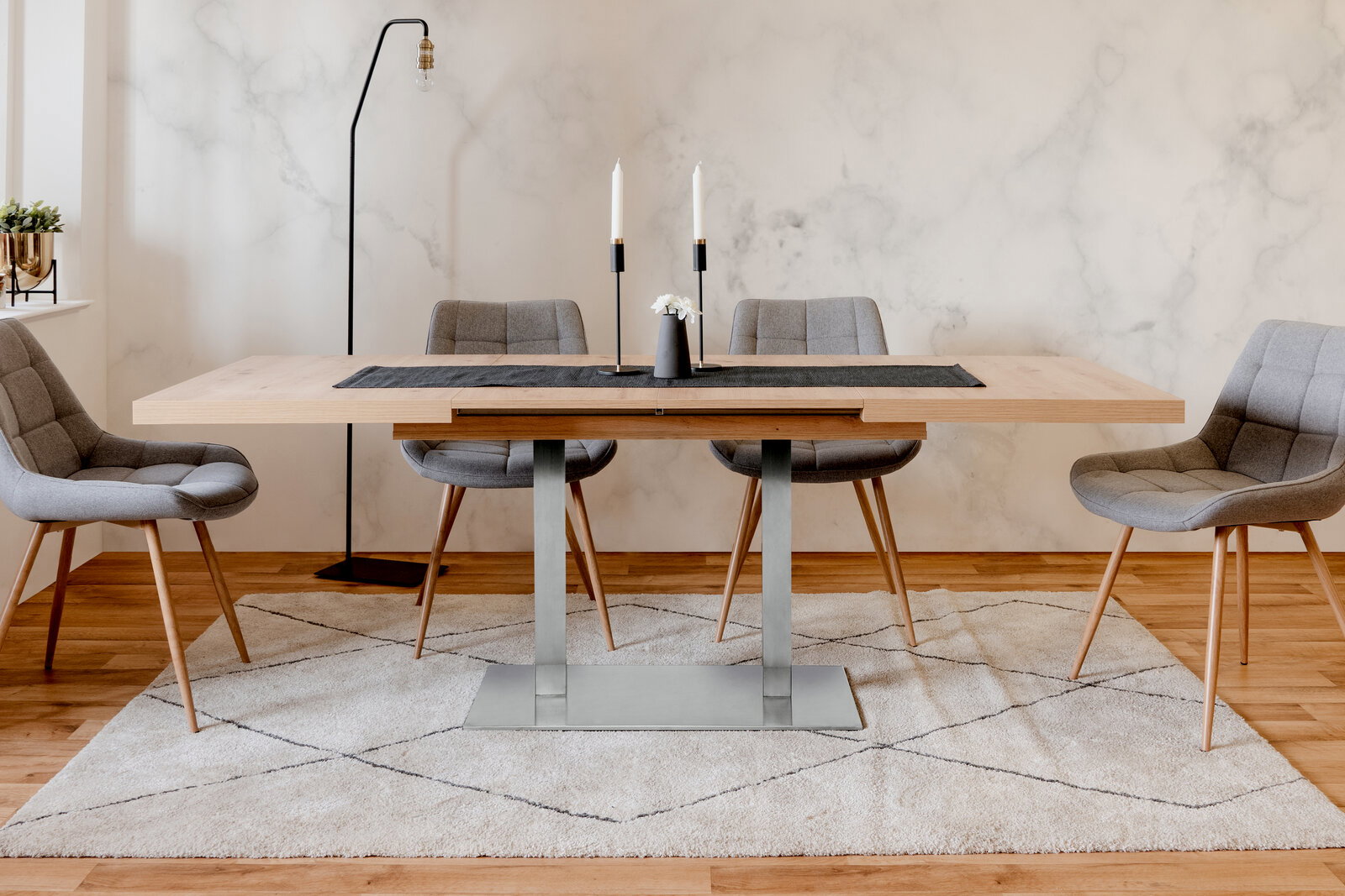 Moderner Esstisch mit Holzplatte und Metallgestell, umgeben von vier grauen Polsterstühlen, in einem stilvoll eingerichteten Raum. Frontalansicht.