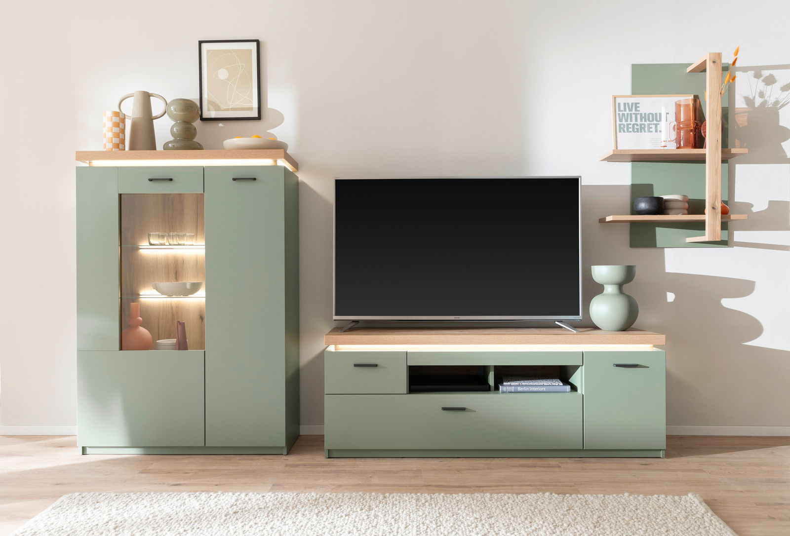 TV-Lowboard in modernem Design, grüne Farbe mit Holzoberfläche, frontal fotografiert, umgeben von dekorativen Elementen und einem Fernseher.