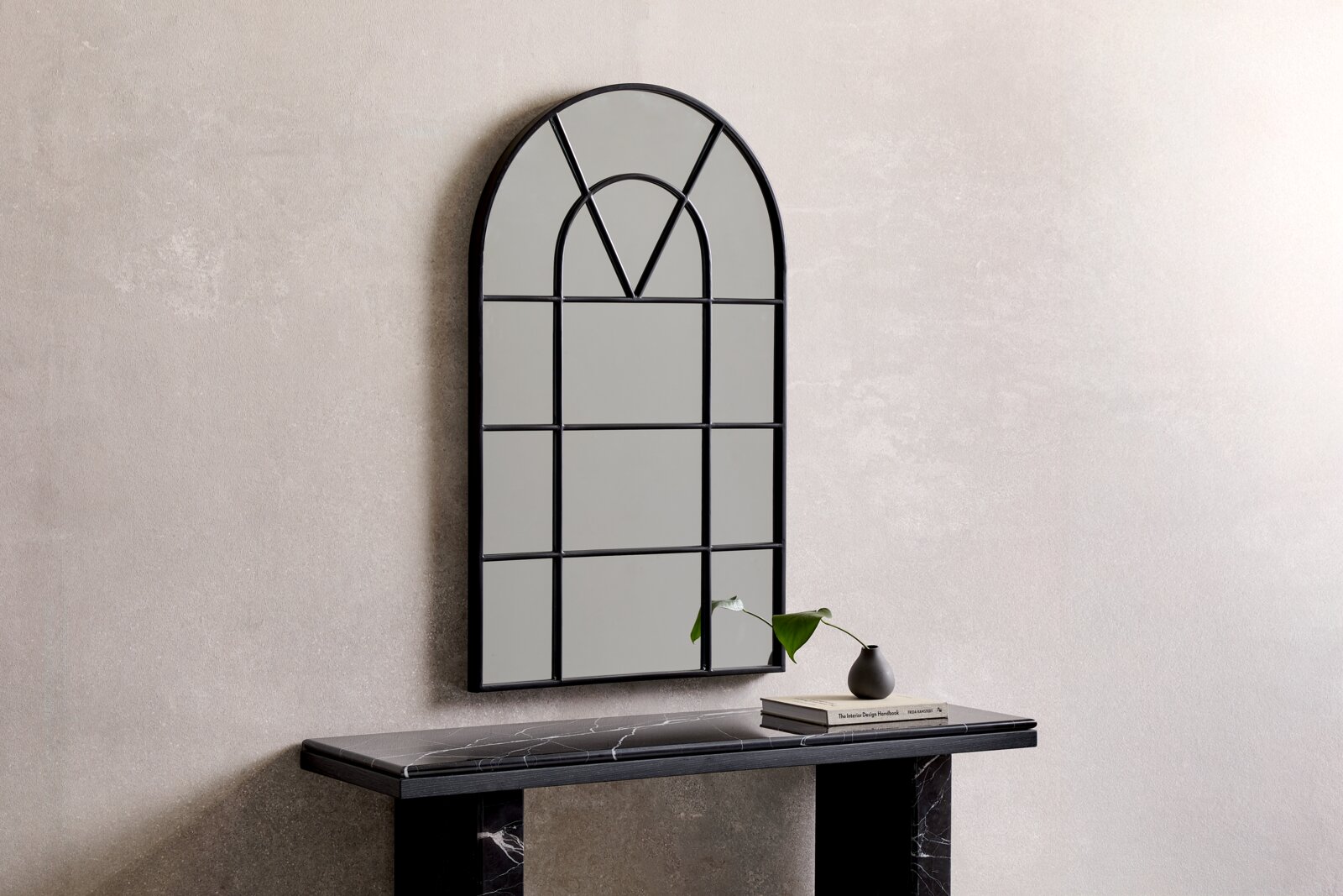 Wandspiegel met een zwarte, gebogen lijst, aan de voorkant opgehangen aan een lichte muur boven een zwarte marmeren tafel met decoratie.