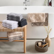 Stilvolle Frottiersets in verschiedenen Farben auf einer Holzbank vor einer Badewanne, mit dekorativen Elementen im Vordergrund, seitliche Perspektive.