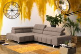 Moderne, graue Rundecke mit Ottomane links in einem stilvoll eingerichteten Wohnzimmer mit Holzboden, gelber Akzentwand, großer Wanduhr und Pflanzen. Perspektive von vorne links.