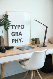 Moderne Schreibtischleuchte in schwarzem Design auf einem Holzschreibtisch, seitliche Perspektive.