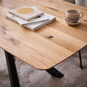 Nahaufnahme eines Esstisches aus Holz mit natürlicher Maserung, darauf liegen Bücher und eine Tasse. Perspektive von schräg oben.