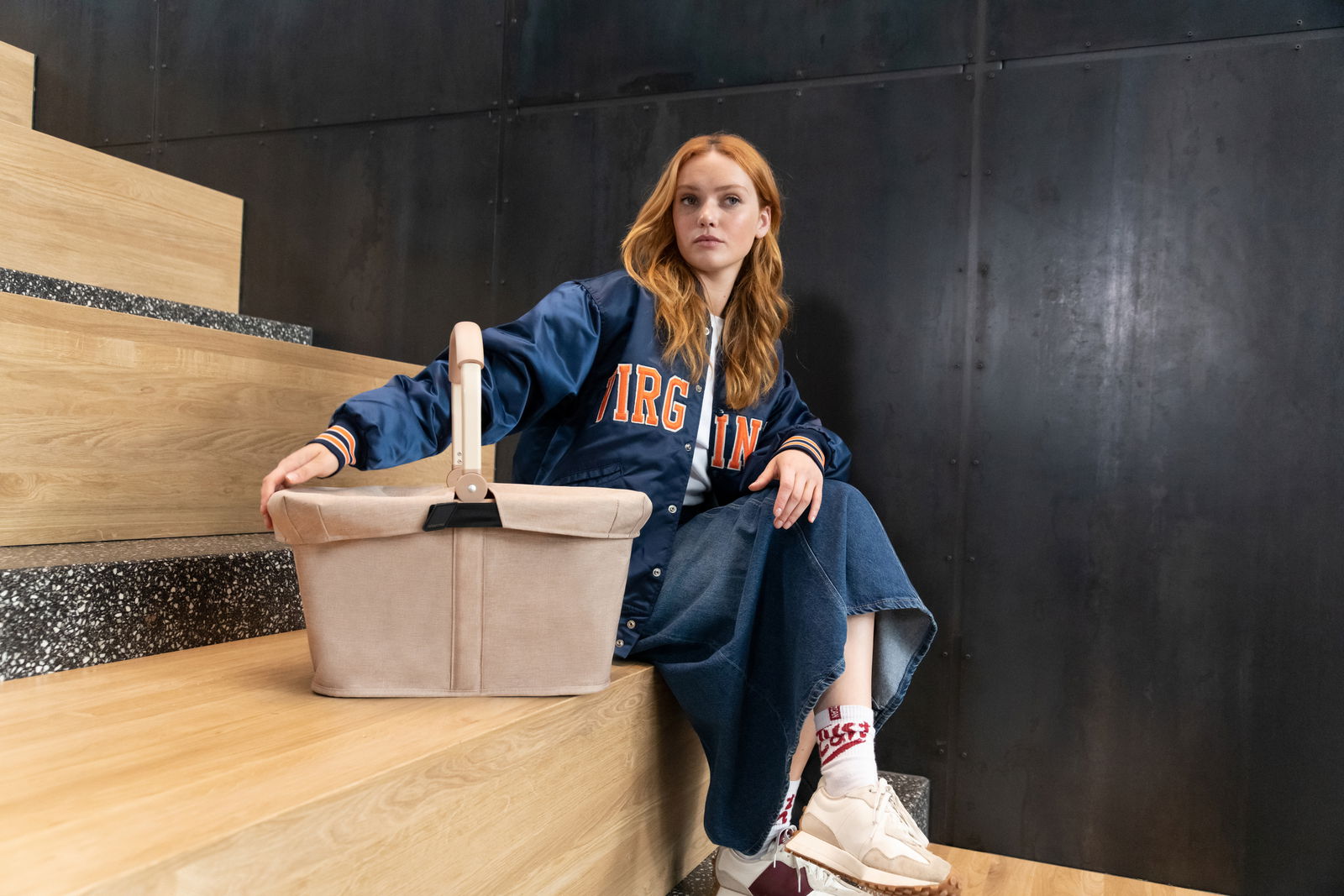 Frau sitzt auf einer Treppe und hält einen beigen Einkaufskorb mit Deckel, seitliche Perspektive