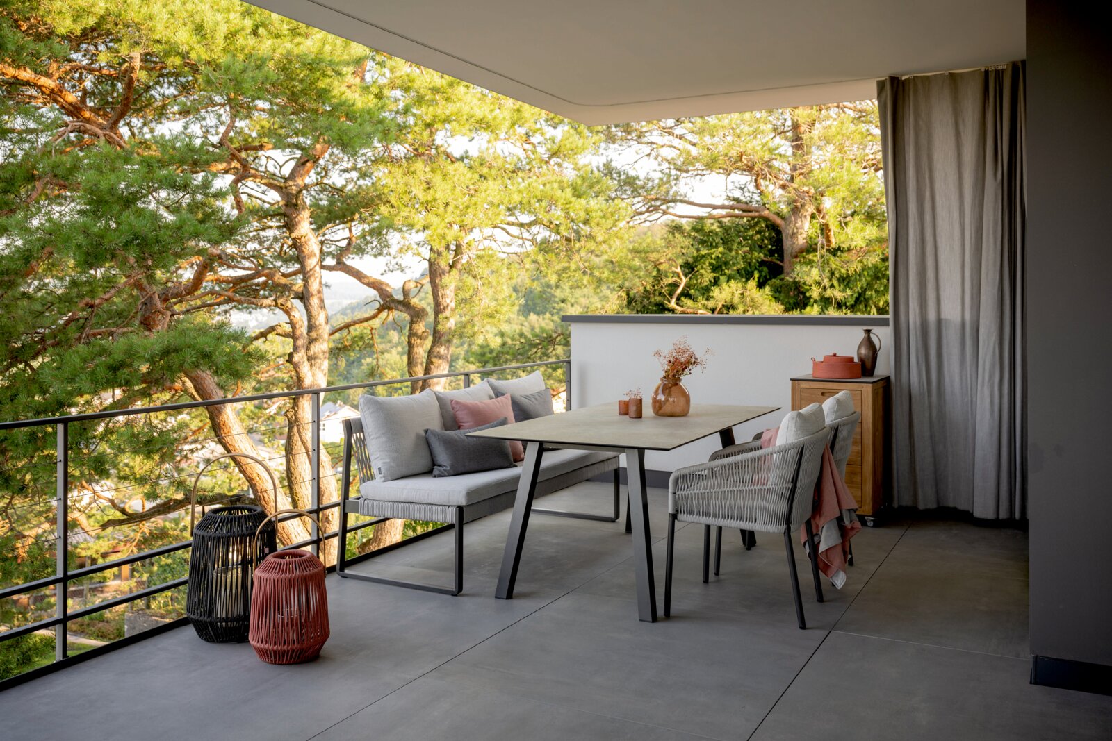 Stern 2-Sitzer Loungelement TAMMO Moderne Balkonmöbel mit einem 2-Sitzer Loungeelement und einem Tisch, umgeben von grünen Bäumen, aus der Perspektive von der Seite aufgenommen.