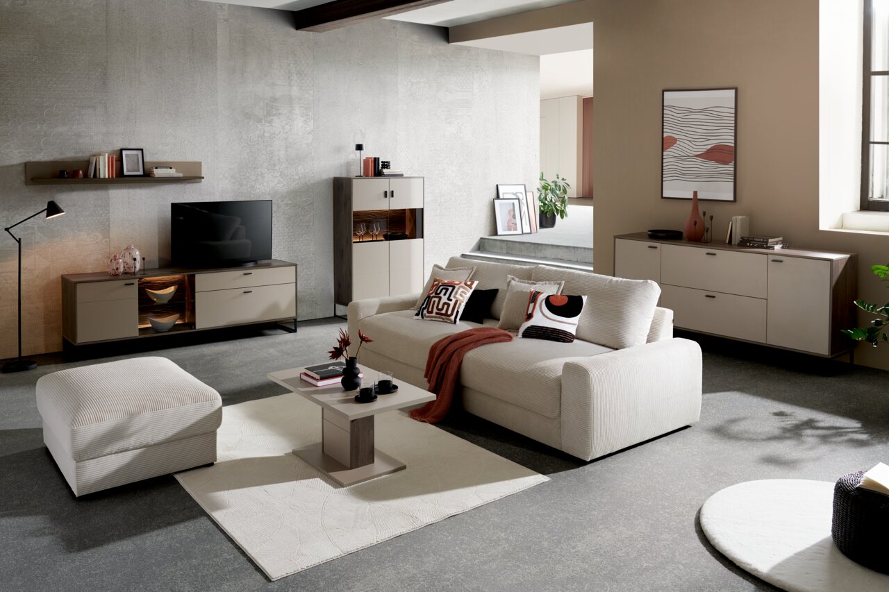 Een moderne woonkamer met een grote, beige bank, versierd met kussens met patronen en een rode deken, gezien vanuit het vooraanzicht.