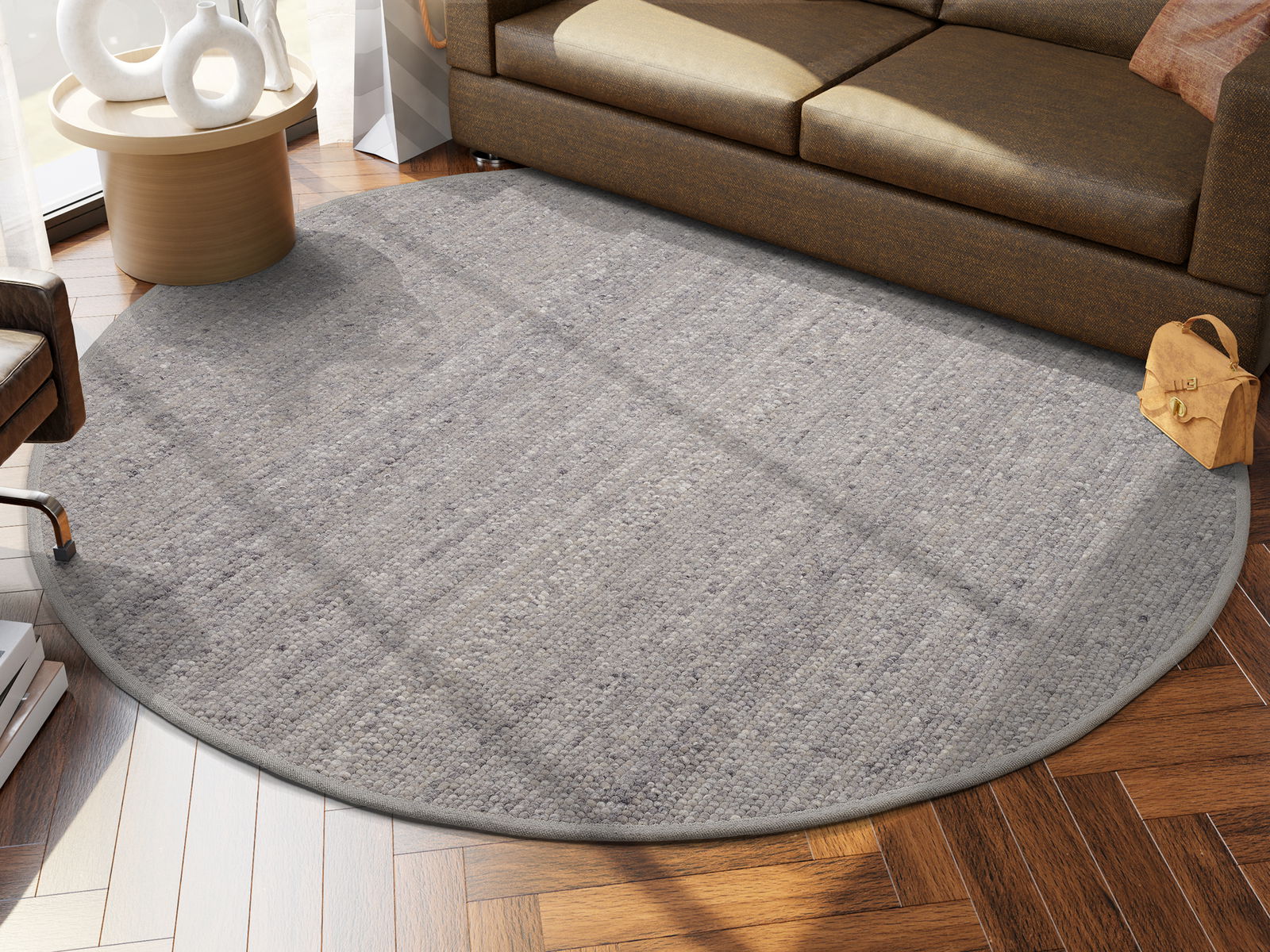 OCI Handweb Teppich FAVORIT Runder, grauer Handwebteppich in einem modernen Wohnzimmer, auf einem Holzboden vor einem braunen Sofa platziert. Perspektive von oben.