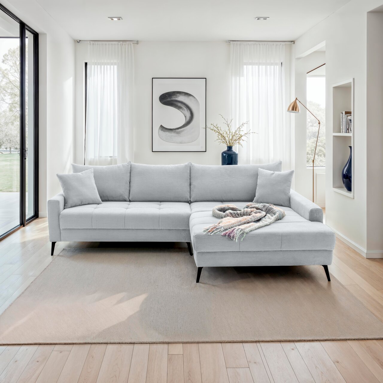 Helles, modernes Ecksofa in einem stilvollen Wohnzimmer, von vorne betrachtet. Das Sofa hat eine L-Form mit einer rechten Ottomane, dekoriert mit einem bunten Überwurf.