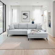 Helles, modernes Ecksofa in einem stilvollen Wohnzimmer, von vorne betrachtet. Das Sofa hat eine L-Form mit einer rechten Ottomane, dekoriert mit einem bunten Überwurf.