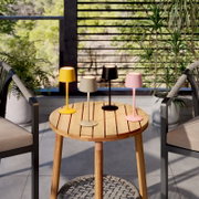 Vier moderne draadloze led-tafellampen in geel, beige, zwart en roze op een ronde houten tafel op het balkon, van voren gefotografeerd vanuit een iets hoger standpunt