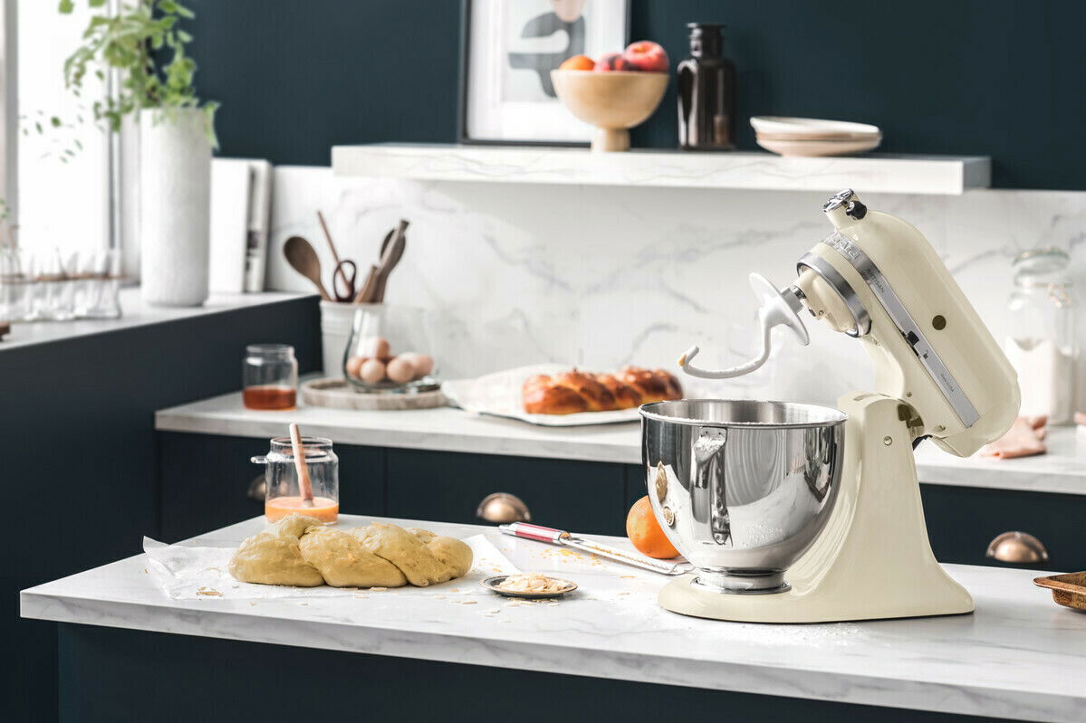 KitchenAid Küchenmaschine 4,8l ARTISAN 5KSM175PSEAC Küchenmaschine 4,8l in Cremefarbe auf einer Küchenarbeitsplatte, seitliche Perspektive, umgeben von Backzutaten.