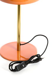 Nahaufnahme einer Tischleuchte mit orangefarbenem Sockel und goldfarbenem Ständer, inklusive schwarzem Kabel mit Schalter.