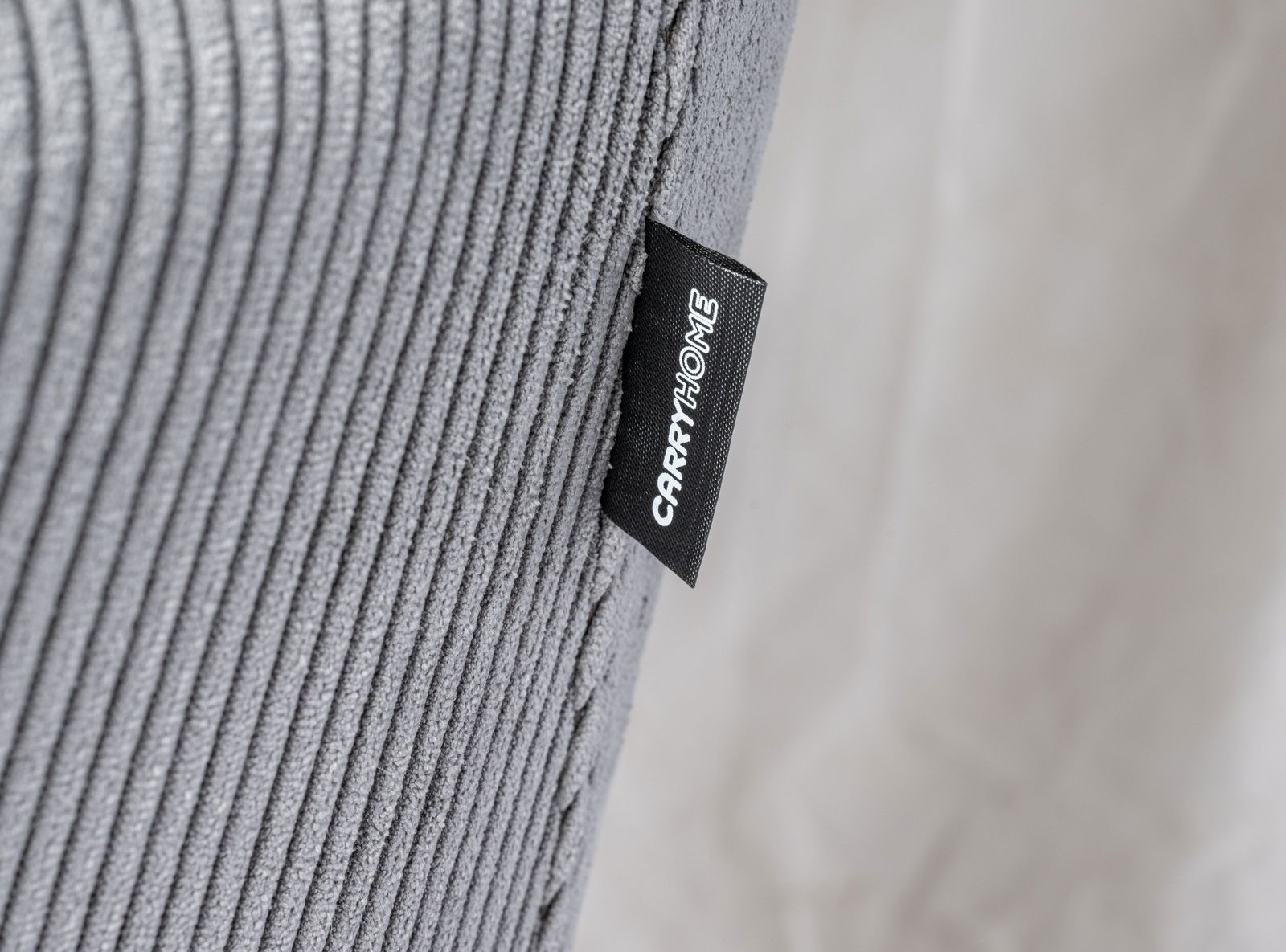 Nahaufnahme eines grauen, gerippten Stoffes mit einem schwarzen Etikett, auf dem 'CARRYHOME' steht, seitliche Perspektive.