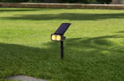 Solarleuchte mit zwei gelben LED-Lichtern und Solarpanel, auf Rasenfläche montiert, seitliche Perspektive