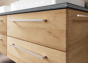 Nahaufnahme einer modernen Badkombination mit Holzoptik und eleganten Metallgriffen, seitliche Perspektive.