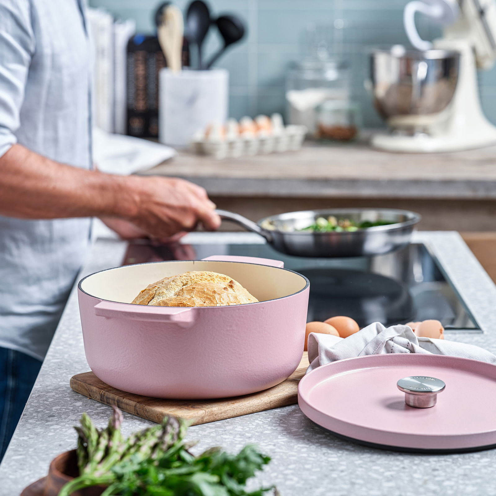 KitchenAid Bräter Runder rosa Gusseisen-Bräter mit Brot, auf einem Schneidebrett in einer modernen Küche, seitliche Perspektive.