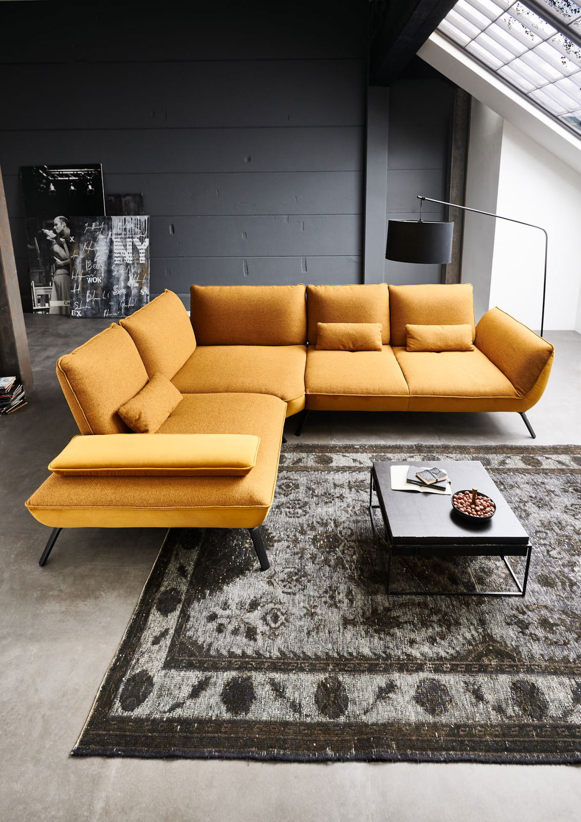 Moderne Eckgarnitur in Senfgelb aus der Vogelperspektive, platziert auf einem gemusterten Teppich neben einem Couchtisch.