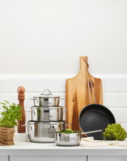 Topfset 5-teilig aus Edelstahl, bestehend aus drei Töpfen mit Deckeln und einer Pfanne, auf einer Küchenarbeitsplatte von vorne fotografiert.