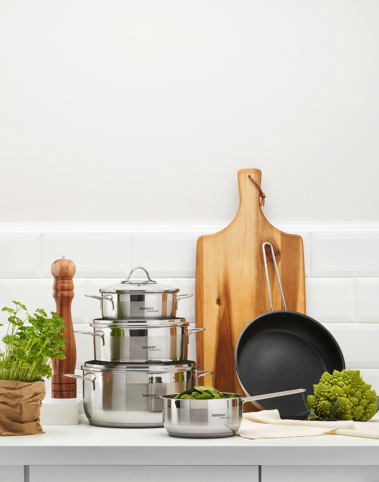 Topfset 5-teilig aus Edelstahl, bestehend aus drei Töpfen mit Deckeln und einer Pfanne, auf einer Küchenarbeitsplatte von vorne fotografiert.