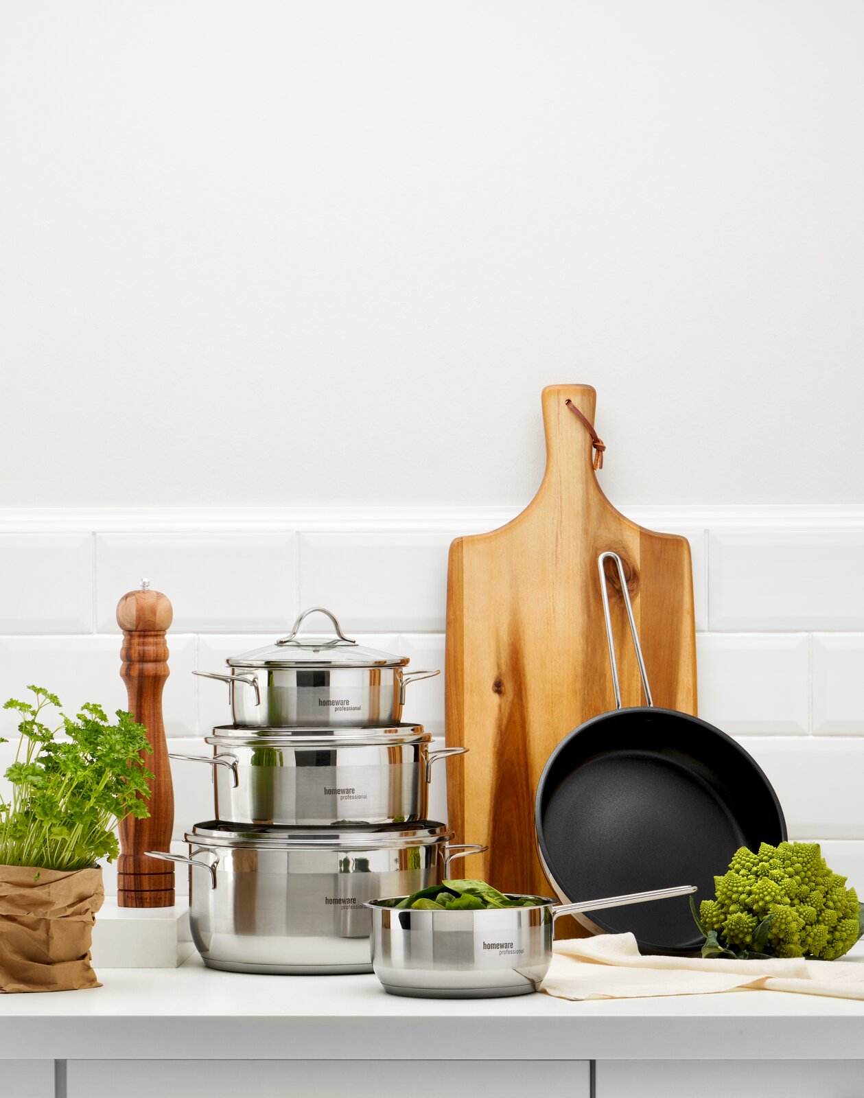 Topfset 5-teilig aus Edelstahl, bestehend aus drei Töpfen mit Deckeln und einer Pfanne, auf einer Küchenarbeitsplatte von vorne fotografiert.