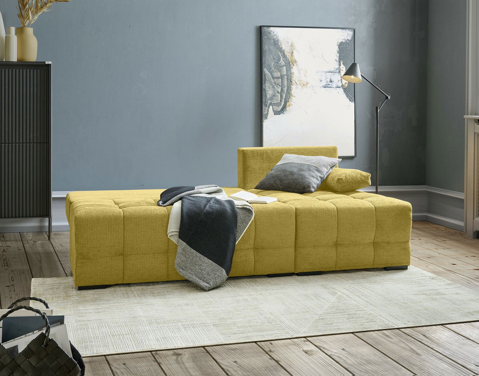 Gelbes Ecksofa MEZZO mit Ottomane rechts, seitliche Perspektive, dekoriert mit Kissen und Decke in modernem Wohnzimmer.