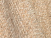 Nahaufnahme eines handgewebten Teppichs mit grober Textur in natürlichen Beigetönen, seitliche Perspektive