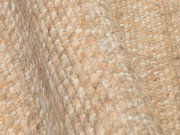 Nahaufnahme eines handgewebten Teppichs mit grober Textur in natürlichen Beigetönen, seitliche Perspektive