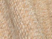 Nahaufnahme eines handgewebten Teppichs mit grober Textur in natürlichen Beigetönen, seitliche Perspektive