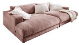 Großes, gemütliches Megasofa in rosa Cordstoff mit mehreren weißen Kissen und einer Decke, seitliche Perspektive