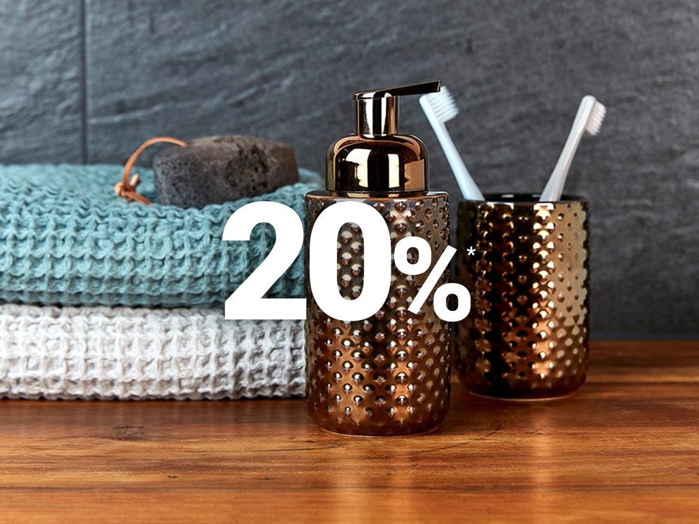 Badezimmer-Setup mit bronzefarbenen Seifenspender und Behälter mit zwei Zahnbürsten, Handtüchern und mit einem „20%“-Rabatttext im Vordergrund.