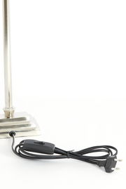 Nahaufnahme eines Lampenfußes aus Nickel mit rechteckiger Basis und einem schwarzen Kabel mit Schalter und Stecker.