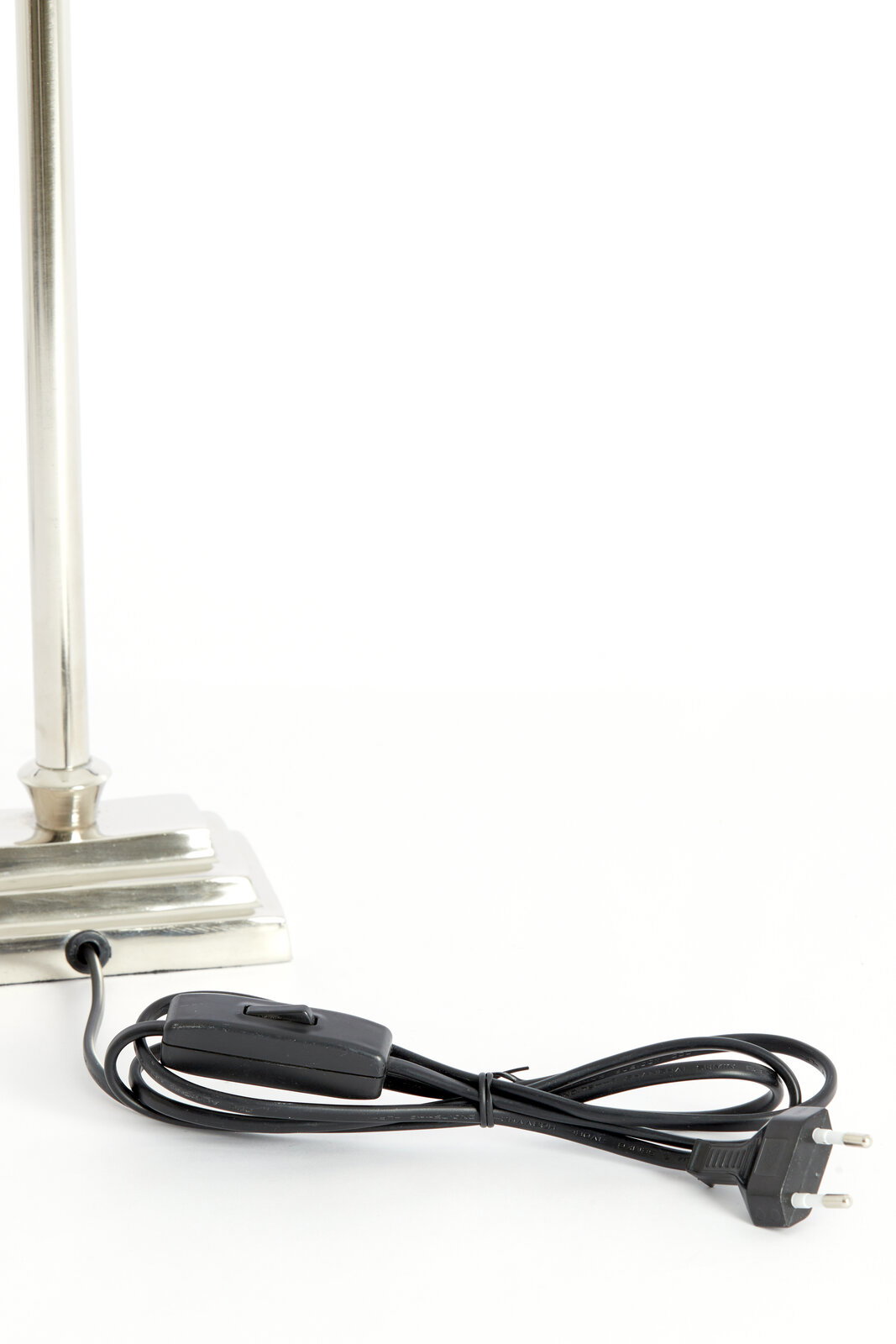 Nahaufnahme eines Lampenfußes aus Nickel mit rechteckiger Basis und einem schwarzen Kabel mit Schalter und Stecker.