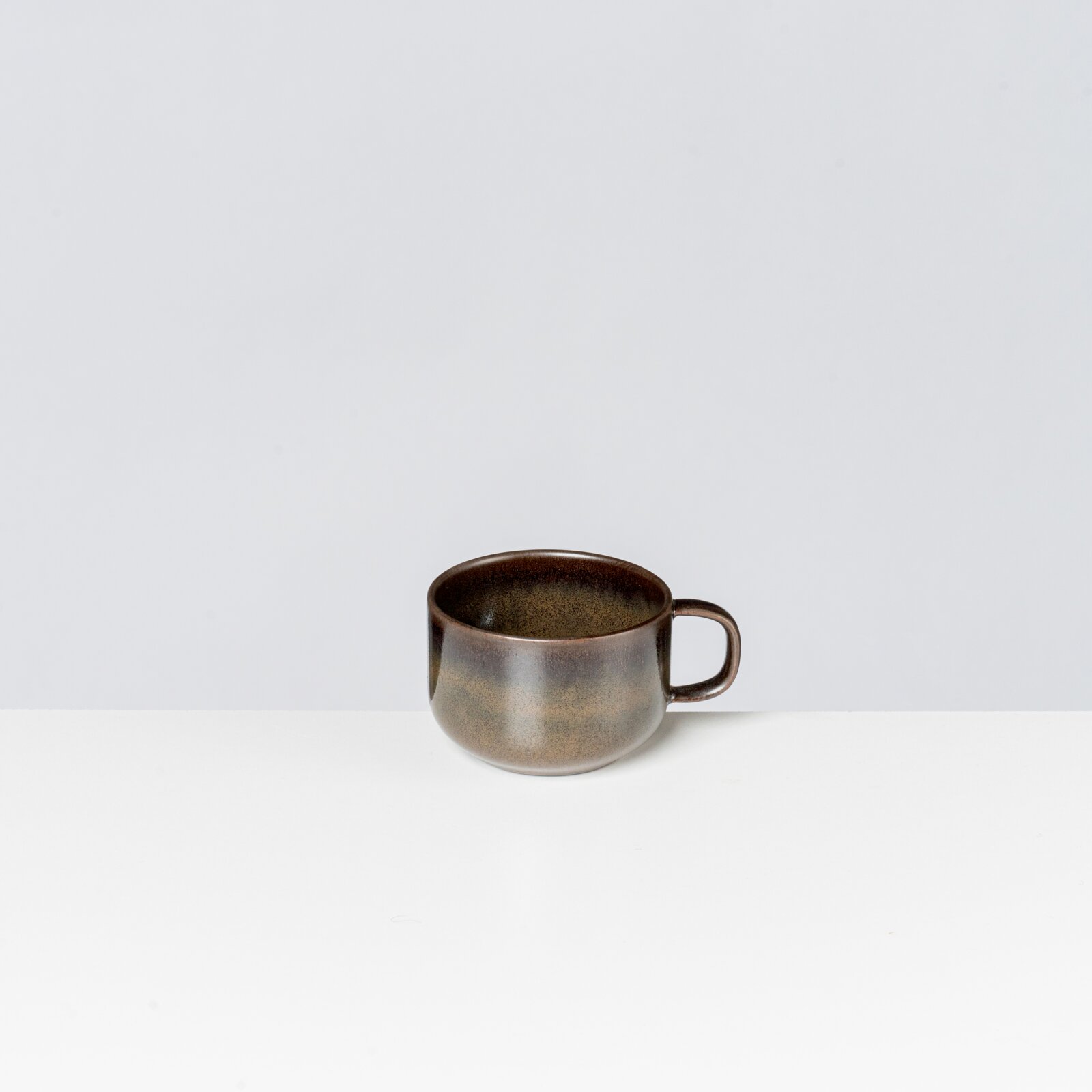 Braune, gesprenkelte Keramik-Tasse mit Henkel auf weißem Hintergrund, leicht von vorne in Seitenansicht fotografiert