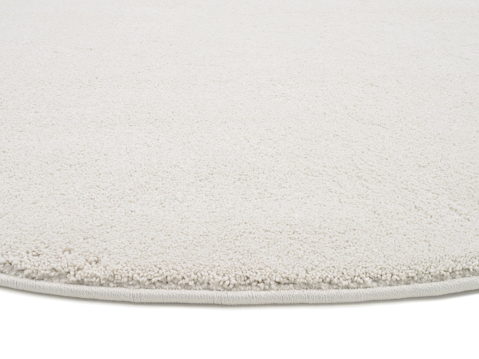 Nahaufnahme eines weißen Uni-Teppichs mit runder Kante, von der Seite betrachtet.