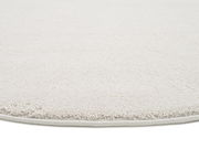 Nahaufnahme eines weißen Uni-Teppichs mit runder Kante, von der Seite betrachtet.