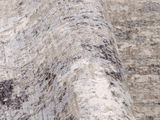 Nahaufnahme eines Designer-Teppichs mit abstraktem Muster in Beige- und Grautönen, aus seitlicher Perspektive aufgenommen.